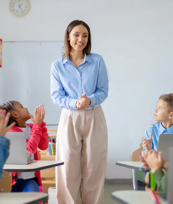 Pupils applaud to female teacher, sitting at desks with laptops, showcasing supportive learning environment where technology meets appreciation for inspiring education